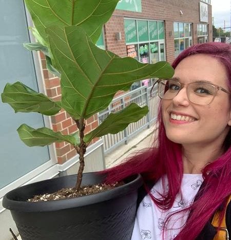 Lacey holds a Fiddle Leaf Fig Plant in her arms with a big smile on her face while standing in front of Bloom 24 Floristry in Halifax.